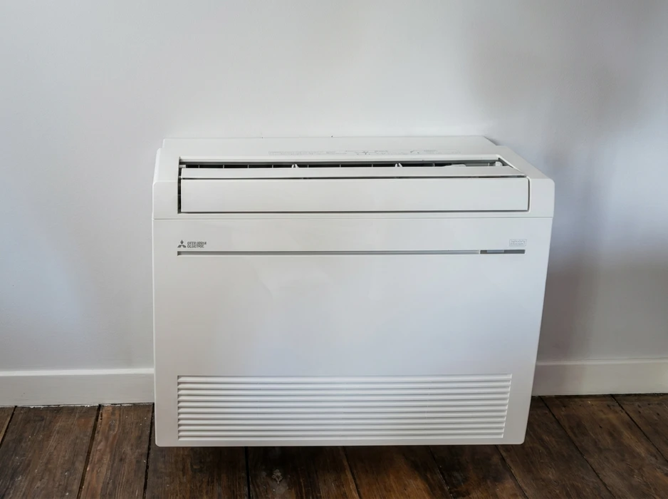 Unité intérieure de climatisation réversible Mitsubishi Electric, modèle console sol-plafond, posée au sol contre un mur blanc