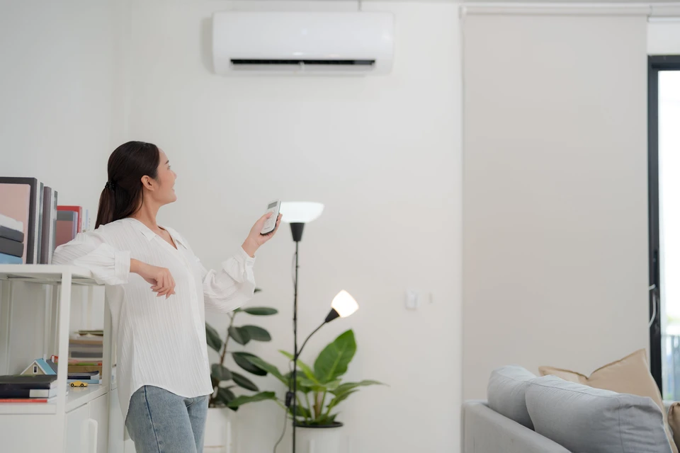 Jeune femme utilise une télécommande pour régler l'air conditionné dans un salon lumineux et moderne à la décoration minimaliste