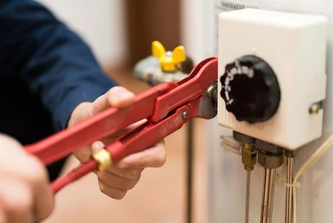 Int&eacute;rieur d'un local technique avec plombier effectuant maintenance sur installation de chauffage