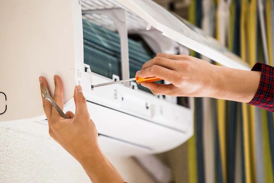 Technicien en combinaison bleue effectuant la maintenance d'une unité de climatisation intérieure