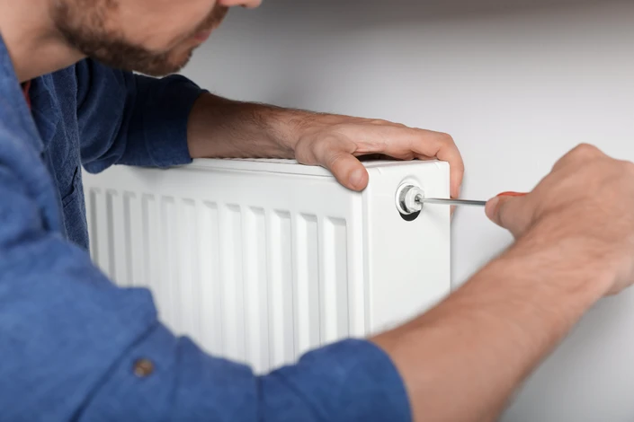Professionnel en chemise à carreaux ajustant une vanne thermostatique sur radiateur à panneaux en acier